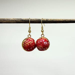 May include: A pair of red and gold dangle earrings with a geometric pattern. The earrings are made of fabric and have a gold hook.