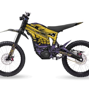 Può includere: Una moto da cross elettrica gialla e viola con la scritta "TRIPLE DESIGN". Ha pneumatici neri, sella nera e grafica con teschio e ossa incrociate. Progettata per l'uso fuoristrada, con un design moderno.