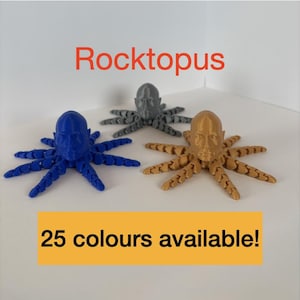 May include: Three 3D-printed octopus figurines in blue, grey, and gold. Each octopus has a human-like face and articulated tentacles. The text "Rocktopus" is above the figurines, and "25 colours available!" is below.