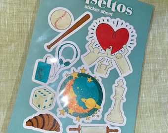 May include: A sticker sheet featuring the text "Falsettos sticker sheet" at the top. The sheet includes a variety of stickers, such as a baseball, a bat, a heart, a cassette tape, headphones, a crescent moon with stars, a dice, a croissant, and a chess piece.