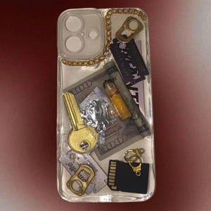 May include: Clear phone case with embedded objects including a gold key, a hundred-dollar bill, a razor blade, a cigarette, and a gold chain. The case also features a gold bottle opener and a black SD card.