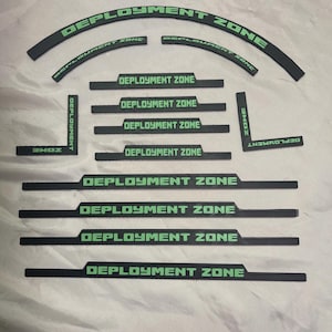 Könnte beinhalten: Ein Satz schwarzer und grüner Vinyl-Aufkleber mit dem aufgedruckten Text "Deployment Zone". Die Aufkleber sind in verschiedenen Formen und Größen, darunter eine gebogene Form und rechteckige Formen.