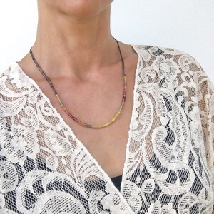 May include: A delicate necklace with small, colorful beads in shades of yellow, orange, and red. The beads are strung on a thin black cord.