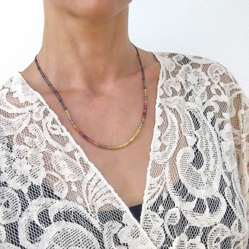 May include: A delicate necklace with small, colorful beads in shades of yellow, orange, and red. The beads are strung on a thin black cord.