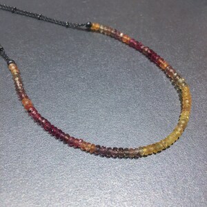 May include: A multi-colored gemstone necklace with a gradient of red, orange, and yellow beads. The necklace is made with a black cord.