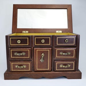 May include: A vintage wooden jewellery box with a hinged mirror. The box has multiple drawers and a central compartment, all decorated with gold-coloured accents. The interior is lined with yellow fabric, offering a classic storage solution.