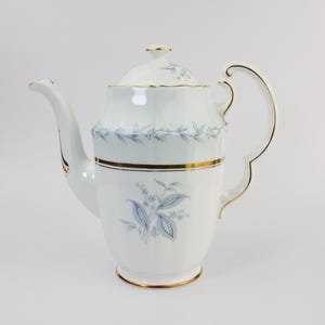 May include: White porcelain teapot with a gold trim and a blue floral pattern. The teapot has a lid and a handle.