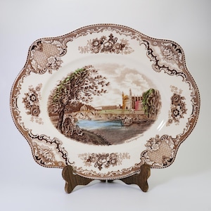 May include: A brown and white oval serving platter with a floral pattern and a scene of a bridge and buildings. The text "Cambridge, England" is printed on the platter.