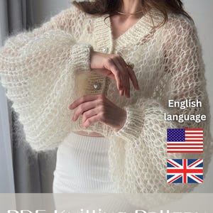 May include: A cream-colored, open-knit cardigan featuring a V-neckline, voluminous balloon sleeves, and heart-shaped buttons. The text on the image reads: English language, PDF KNITTING PATTERN, LACE cardigan, along with US and UK flag icons.