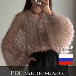 Può includere: Un cardigan corto in mohair rosa chiaro a maglia larga, con maniche lunghe e voluminose, scollo a V e tre bottoni dorati a forma di cuore. L'immagine include il testo "Русский язык", una bandiera russa e "PDF МАСТЕР-класс кардиган LACE".