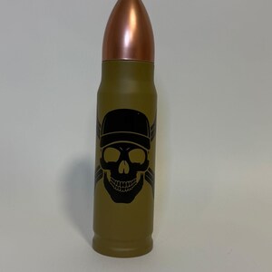 Könnte beinhalten: Eine grüne, kugelförmige Wasserflasche mit einem schwarzen Totenkopf- und Knochenkreuz-Design. Der Totenkopf trägt eine schwarze Baseballkappe.