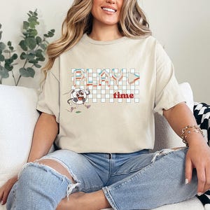 May include: A beige t-shirt with a pixelated graphic of a soccer ball and the text "PLAY time".