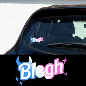 May include: A car window sticker with the word "Blegh" in a stylized font. The word is in white with a blue and pink gradient, and is decorated with a devil horn graphic and starbursts.