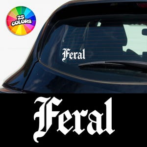 May include: White vinyl decal with the word "Feral" in a gothic font. The decal is applied to the rear window of a black car.