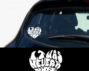 May include: White vinyl decal in the shape of a heart with the words "It Was Never a Phase" written inside. The decal is on the back window of a black car.