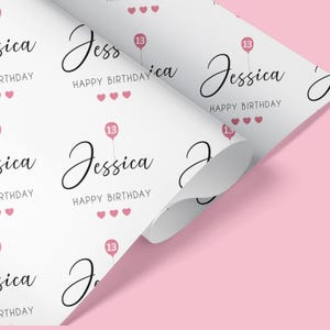 May include: White wrapping paper with a repeating pattern of pink hearts, the name "Jessica" in cursive, the words "Happy Birthday", and a pink balloon with the number "13" printed on it.