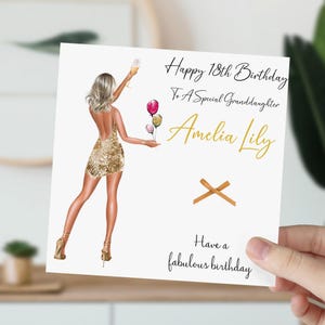 May include: A white card with gold lettering that says "Happy 18th Birthday To A Special Granddaughter Amelia Lily Have a fabulous birthday". The card features a gold glitter dress and a woman holding a glass of champagne and balloons.
