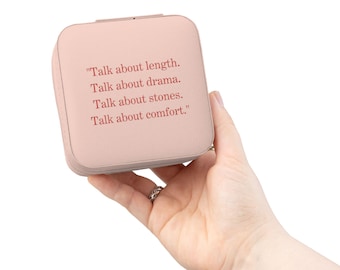 Può includere: Un portagioie quadrato rosa cipria con una cerniera argentata, tenuto in mano. Il portagioie presenta il testo "Talk about length. Talk about drama. Talk about stones. Talk about comfort." in rosso.