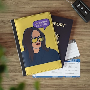 May include: A yellow and black passport holder with an illustration of a woman wearing glasses and the text "Oh my God, I'm in 17C." is next to a passport and two boarding passes. A car key is in the background.