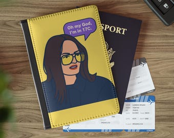 Può includere: Un porta passaporto giallo e nero con un'illustrazione di una donna con gli occhiali e il testo "Oh my God, I'm in 17C." è accanto a un passaporto e due carte d'imbarco. Una chiave dell'auto è sullo sfondo.