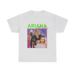 Könnte beinhalten: Ein graues T-Shirt mit einem Grafikdruck von Ariana Grande und dem Text "Ariana Grande" in grünen Buchstaben.