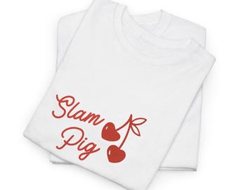 Può includere: Due magliette bianche sono impilate, con la maglietta superiore con il testo rosso "Slam Pig" e una grafica di ciliegie. Le magliette sono piegate con cura, mostrando il design in modo prominente. Il design include due ciliegie a forma di cuore.