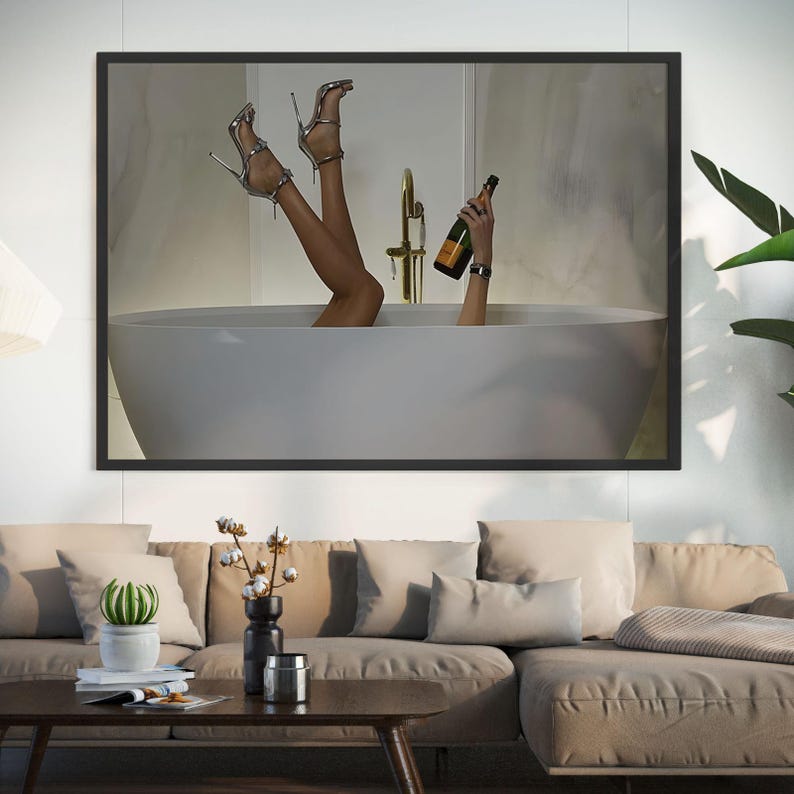 Op de afbeelding: Een ingelijste print met een persoon in een witte badkuip met zilveren hoge hakken en een champagnefles. De afbeelding heeft een moderne, luxe uitstraling, met een gouden kraan en een neutraal kleurenpalet.