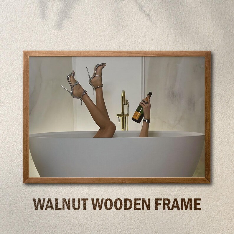 Op de afbeelding: Een ingelijste afbeelding van een persoon in een bad, met de benen omhoog, met zilveren hoge hakken. Een hand houdt een champagnefles vast. De lijst is van walnotenhout, met de tekst "WALNUT WOODEN FRAME" onderaan.
