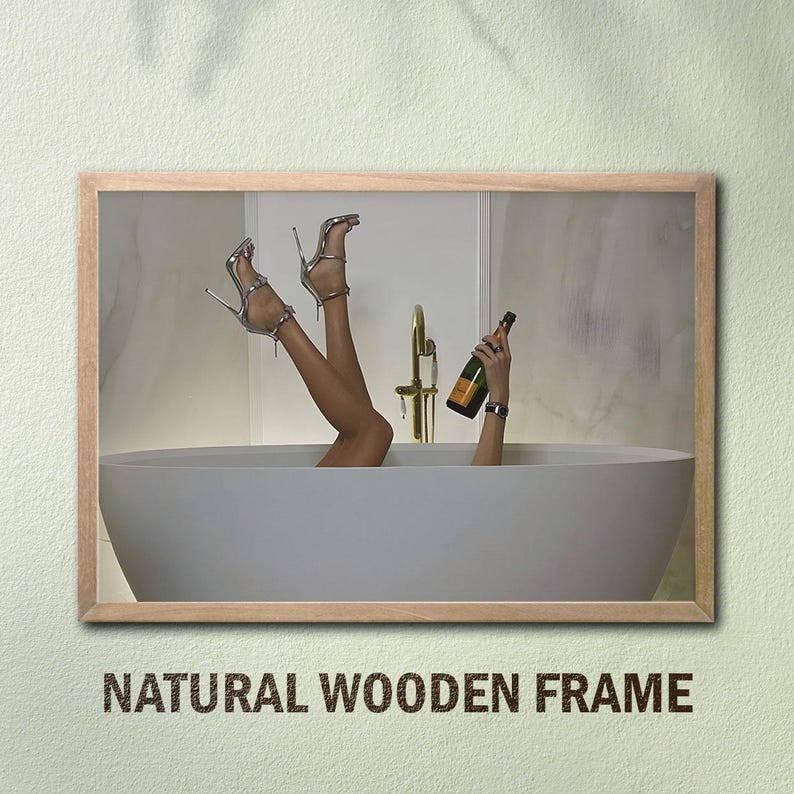 Op de afbeelding: Een ingelijste afbeelding met een persoon in een badkuip met omhooggestoken benen, zilveren hoge hakken en een champagnefles. De afbeelding is ingelijst met een natuurlijke houten lijst. De tekst "NATURAL WOODEN FRAME" staat onderaan.