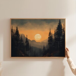 May include: A framed landscape art print depicting a sunset over a forest. The artwork features silhouetted evergreen trees, a bright yellow sun, and a gradient sky of orange and gray hues. The frame is made of light-colored wood.