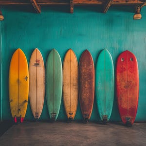 May include: Seven surfboards of varying colors, including yellow, beige, green, and red, are lined up against a teal wall. The surfboards have a classic longboard shape and show signs of wear, suggesting they have been used.
