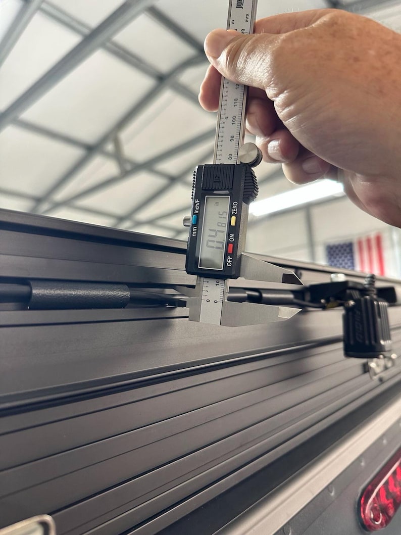 May include: A digital caliper measuring the thickness of a black, grooved surface. The caliper reads 0.4815 inches. The image shows a close-up of the measurement process, highlighting the precision of the tool.