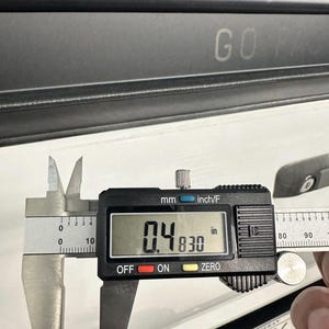 May include: A digital caliper measuring 0.4830 inches. The caliper is black and silver, with a digital display showing the measurement. The text "GO FAST" is visible in the background.
