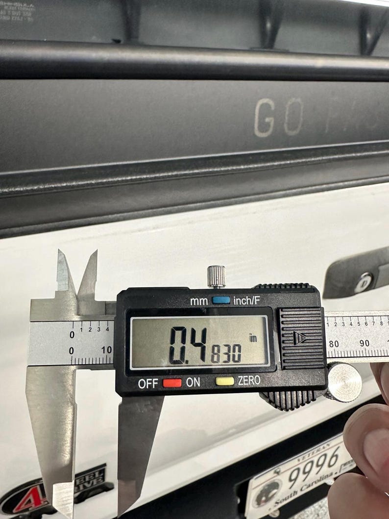 May include: A digital caliper measuring 0.4830 inches. The caliper is black and silver, with a digital display showing the measurement. The text "GO FAST" is visible in the background.