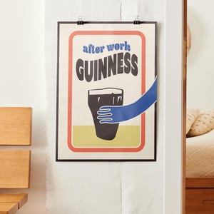 Op de afbeelding: Een poster in vintage stijl met een zwarte rand en rode, oranje en gele accenten. De poster toont een glas Guinness-bier met een blauwe hand die ernaar reikt. De tekst op de poster luidt "after work GUINNESS".