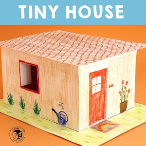May include: A papercraft model of a tiny house with a red door, a window, and a brown roof. The house is sitting on a green lawn with a watering can and flowers.