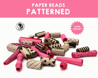 May include: A collection of patterned paper beads in pink and brown with black geometric designs. The beads are made of rolled paper and are perfect for jewelry making.