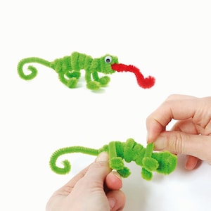 May include: Two green pipe cleaner chameleon crafts. One chameleon has a red pipe cleaner tongue. The other chameleon is being held by a hand.