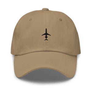 May include: A tan baseball cap with a black airplane graphic on the front. The cap has a curved brim and an adjustable strap at the back. The hat is made of a soft, durable material.