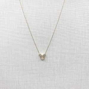 K&ouml;nnte beinhalten: Eine goldfarbene Halskette mit einem Anh&auml;nger in Form eines Cartoon-Mauskopfes. Der Anh&auml;nger ist mit kleinen, klaren Kristallen besetzt. Die zarte Kette h&auml;ngt vor einem neutralen Hintergrund.