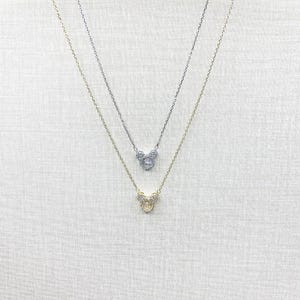 K&ouml;nnte beinhalten: Zwei zarte Halsketten mit Anh&auml;ngern in Form eines M&auml;usekopfes. Eine Halskette ist silberfarben, die andere goldfarben. Die Anh&auml;nger und Ketten sind mit kleinen, funkelnden Steinen besetzt, was einen glamour&ouml;sen Look erzeugt.