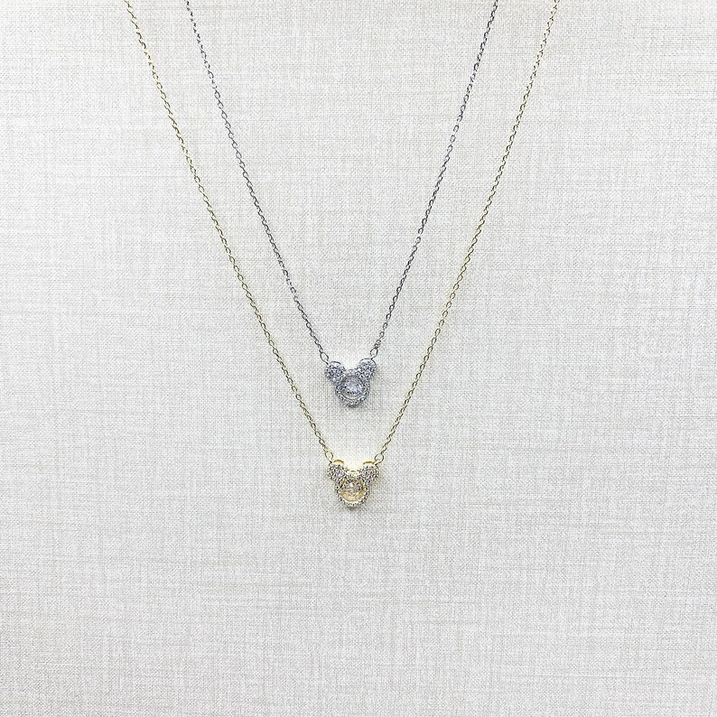 K&ouml;nnte beinhalten: Zwei zarte Halsketten mit Anh&auml;ngern in Form eines M&auml;usekopfes. Eine Halskette ist silberfarben, die andere goldfarben. Die Anh&auml;nger und Ketten sind mit kleinen, funkelnden Steinen besetzt, was einen glamour&ouml;sen Look erzeugt.