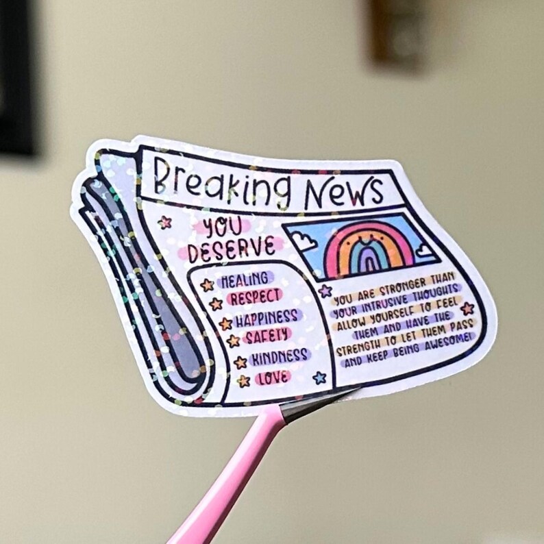 May include: A sticker with a newspaper design that says "Breaking News: You Deserve" with a rainbow and a list of positive affirmations including healing, respect, happiness, safety, kindness, and love. The sticker has a glittery finish.