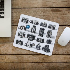 以下が含まれることがあります： 白の マウスパッド に、白黒のヴィンテージカメラのコレクションが並んでいます。カメラはグリッド状に配置されており、形やサイズがそれぞれ異なります。