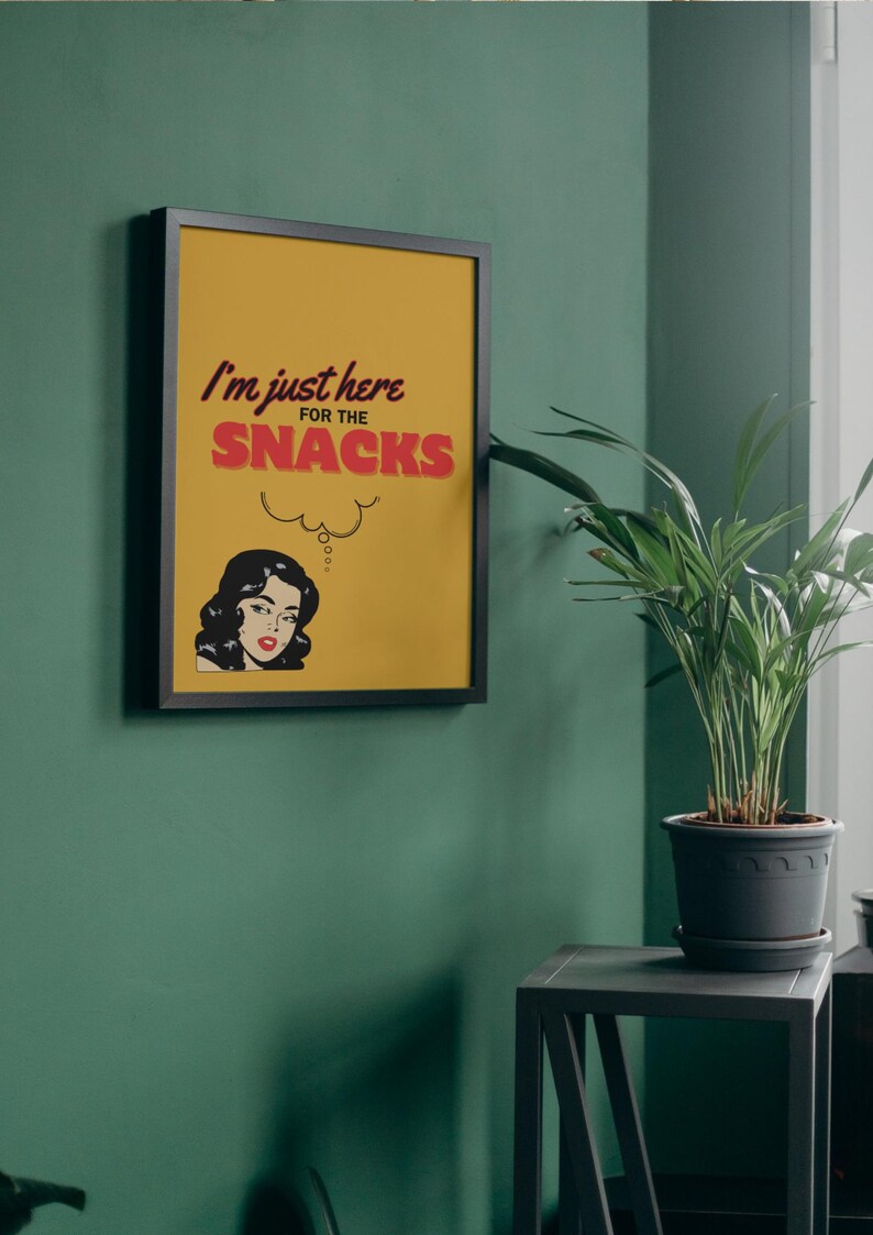 May include: A framed print with a yellow background and black frame. The print features a woman with black hair and a red dress, thinking about snacks. The text reads "I'm just here for the snacks".