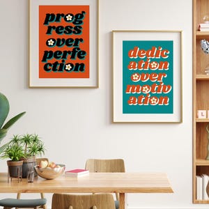 May include: Two framed prints with motivational quotes in a retro style. The print on the left has an orange background with the text "progress over perfection" in black with white flowers. The print on the right has a teal background with the text "dedication over motivation" in black with white flowers.