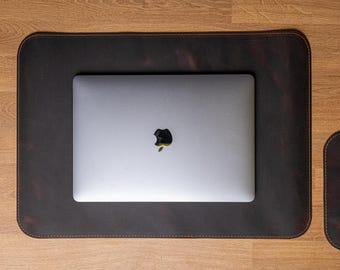 May include: A brown leather desk mat with a laptop computer on top. The laptop has a silver case and an apple logo.