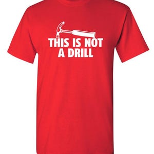 May include: A red t-shirt with a white graphic of a hammer and the text "THIS IS NOT A DRILL". The short-sleeved shirt is made of a soft material and is suitable for casual wear.