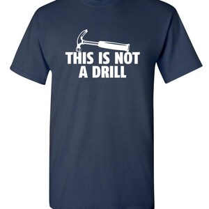 May include: Navy blue t-shirt with a white graphic of a hammer and the text "THIS IS NOT A DRILL". The short-sleeved shirt is made of a soft material.