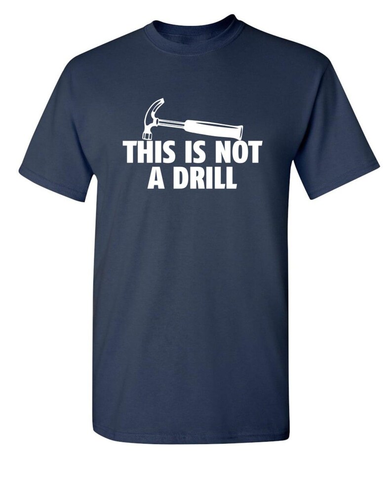 May include: Navy blue t-shirt with a white graphic of a hammer and the text "THIS IS NOT A DRILL". The short-sleeved shirt is made of a soft material.